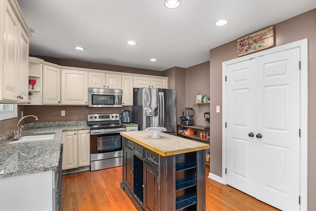 kitchen featuring appliances with stainless steel finishes, sink, butcher block countertops, a center island, and light hardwood / wood-style flooring