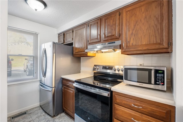 kitchen with appliances with stainless steel finishes, light tile patterned flooring, decorative backsplash, and a textured ceiling