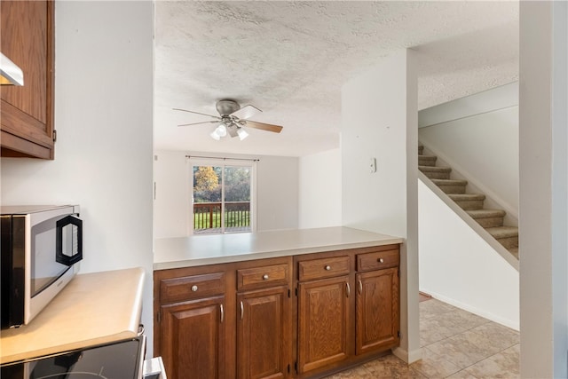 kitchen with kitchen peninsula, stainless steel appliances, light tile patterned floors, a textured ceiling, and ceiling fan