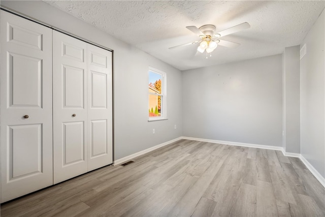 unfurnished bedroom featuring light hardwood / wood-style flooring, a textured ceiling, a closet, and ceiling fan