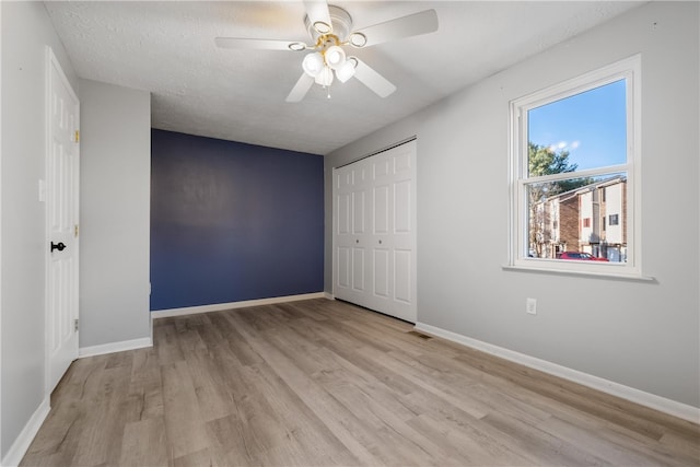 unfurnished bedroom with light hardwood / wood-style floors, a closet, a textured ceiling, and ceiling fan