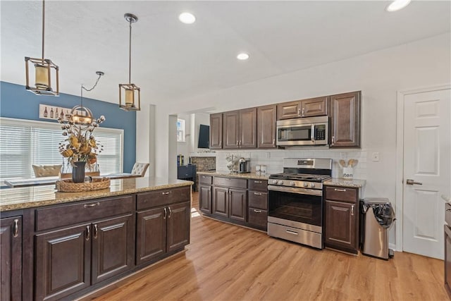 kitchen with dark brown cabinets, stainless steel appliances, decorative light fixtures, and light wood-type flooring