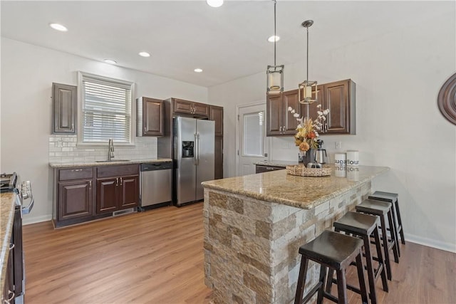 kitchen featuring sink, a breakfast bar area, decorative light fixtures, light hardwood / wood-style floors, and stainless steel appliances