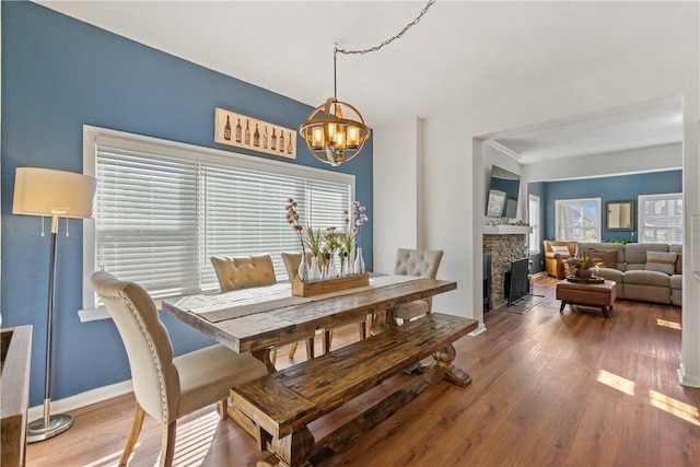 dining space featuring a stone fireplace, a wealth of natural light, a notable chandelier, and hardwood / wood-style flooring