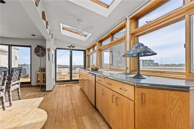 kitchen with ceiling fan, vaulted ceiling with skylight, light hardwood / wood-style flooring, and plenty of natural light