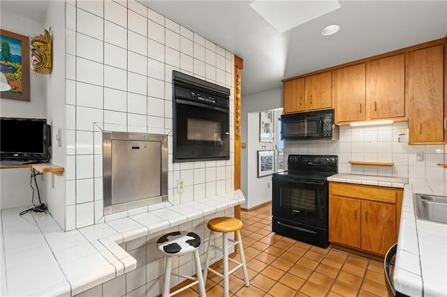 kitchen with tile countertops, black appliances, and backsplash