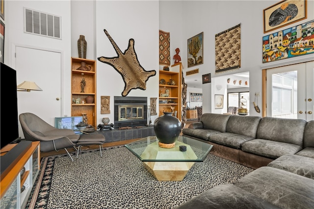 living room with french doors, a tiled fireplace, a high ceiling, and built in shelves