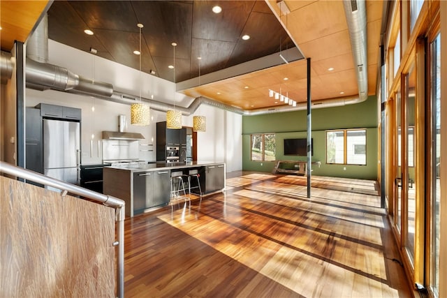 kitchen with a spacious island, a kitchen bar, light wood-type flooring, stainless steel refrigerator, and a towering ceiling