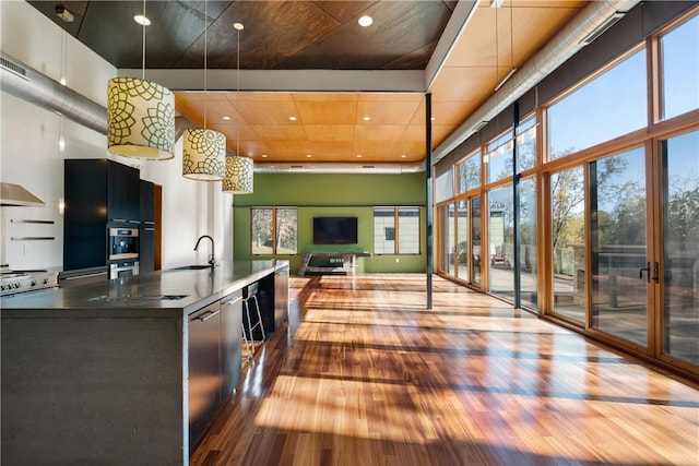 kitchen with a towering ceiling, sink, pendant lighting, and hardwood / wood-style floors