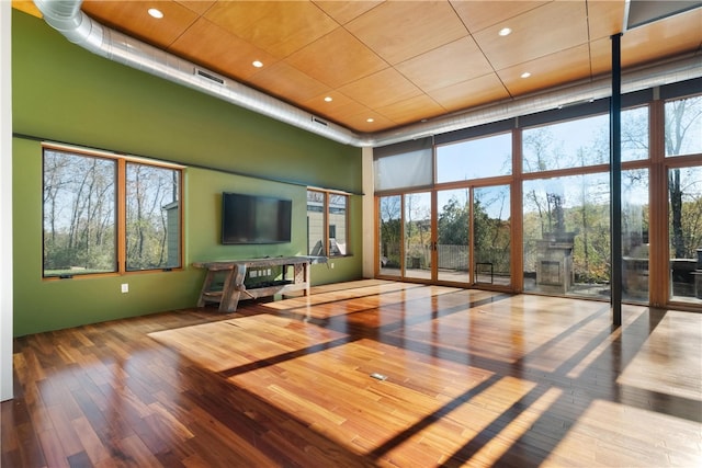 unfurnished living room featuring a towering ceiling, hardwood / wood-style flooring, and a healthy amount of sunlight