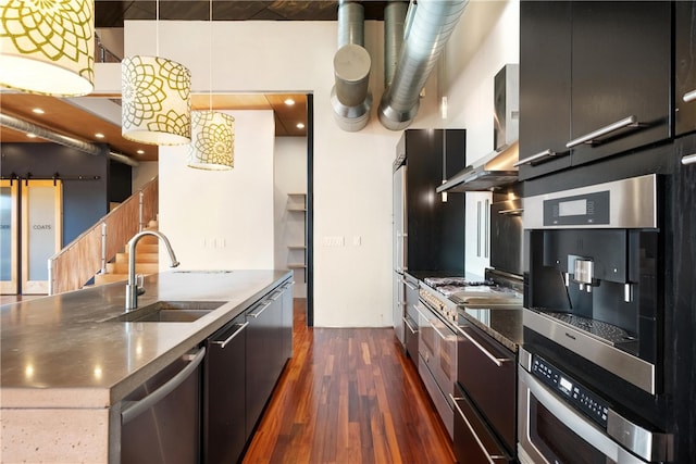 kitchen with a center island with sink, sink, a barn door, pendant lighting, and dark hardwood / wood-style flooring