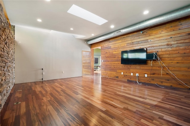 unfurnished living room featuring a skylight, wooden walls, and hardwood / wood-style floors