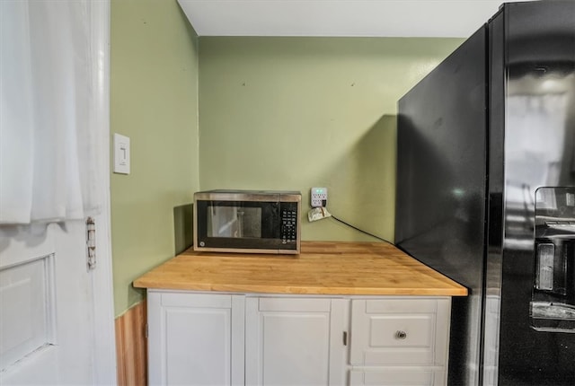 kitchen with white cabinetry, butcher block countertops, and black refrigerator with ice dispenser