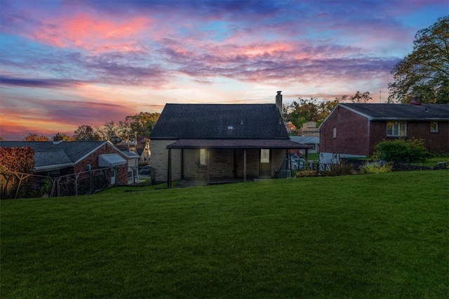 back house at dusk featuring a lawn