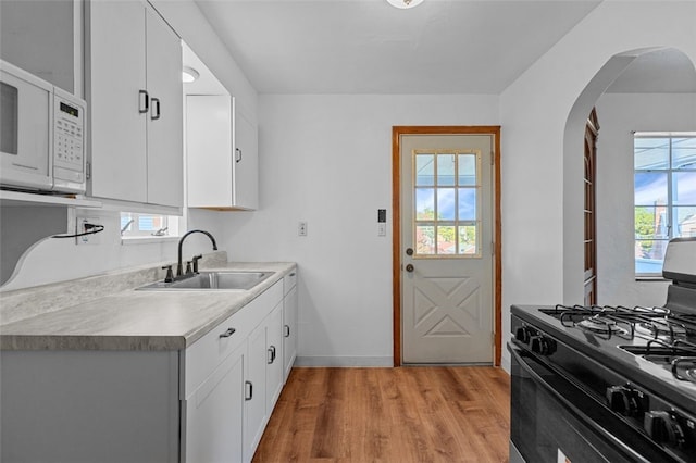 kitchen with black range with gas cooktop, sink, white cabinetry, and light hardwood / wood-style flooring