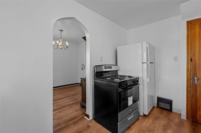 kitchen with an inviting chandelier, hardwood / wood-style floors, black gas range oven, and white refrigerator