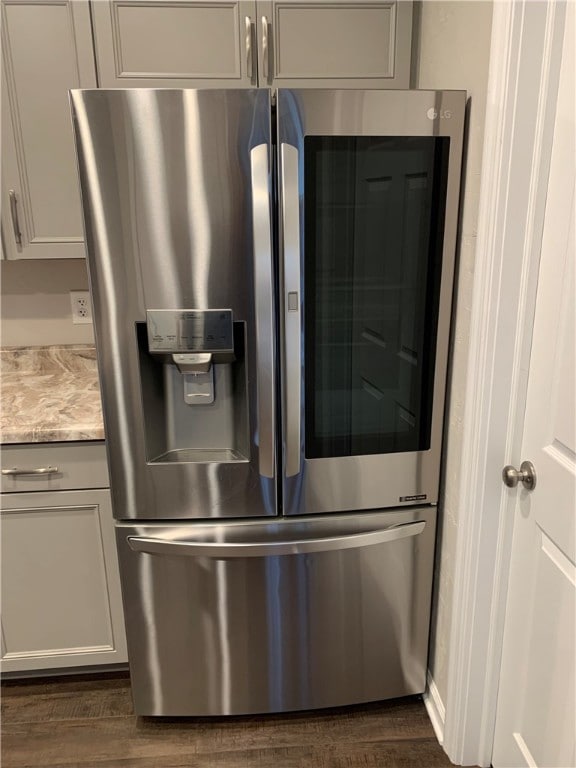 details featuring dark wood-type flooring, light stone counters, and stainless steel fridge