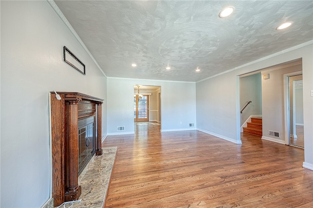 unfurnished living room with light hardwood / wood-style floors, ornamental molding, a textured ceiling, a notable chandelier, and a high end fireplace