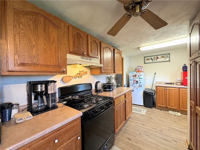 kitchen featuring light wood-type flooring, black gas range oven, white fridge, a textured ceiling, and ceiling fan