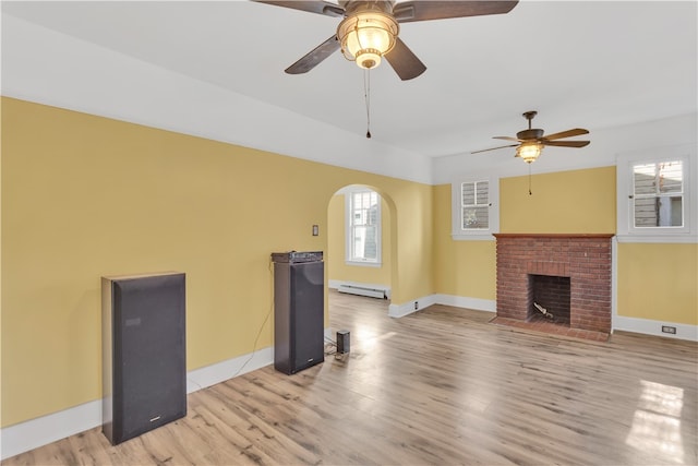 unfurnished living room with baseboard heating, a fireplace, light wood-type flooring, and ceiling fan