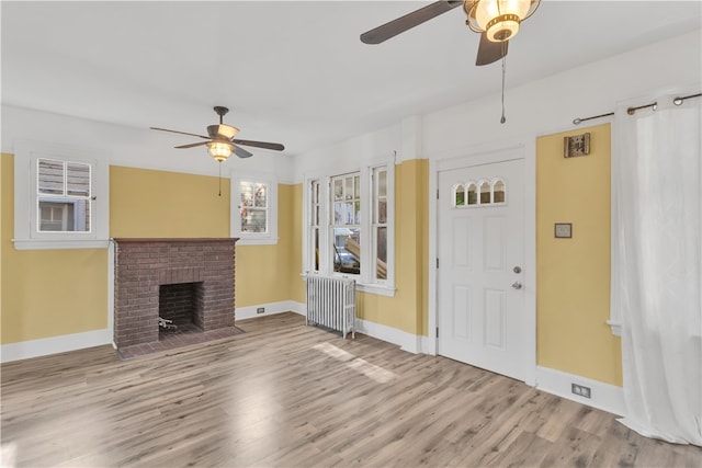 unfurnished living room with a fireplace, radiator heating unit, light wood-type flooring, and ceiling fan