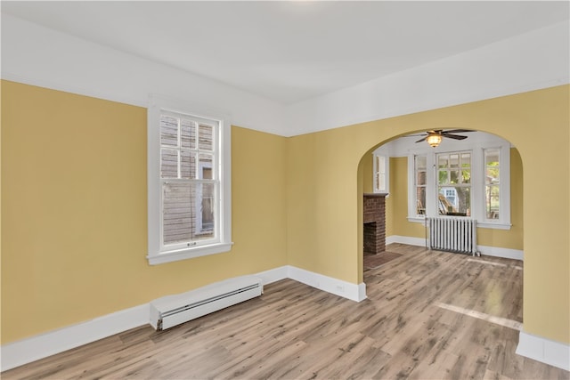 empty room featuring radiator heating unit, a baseboard heating unit, ceiling fan, light wood-type flooring, and a fireplace