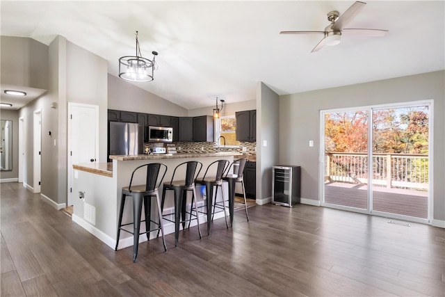 kitchen with decorative backsplash, a breakfast bar area, stainless steel appliances, vaulted ceiling, and dark hardwood / wood-style flooring