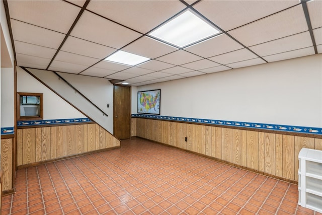 basement with a paneled ceiling and wood walls