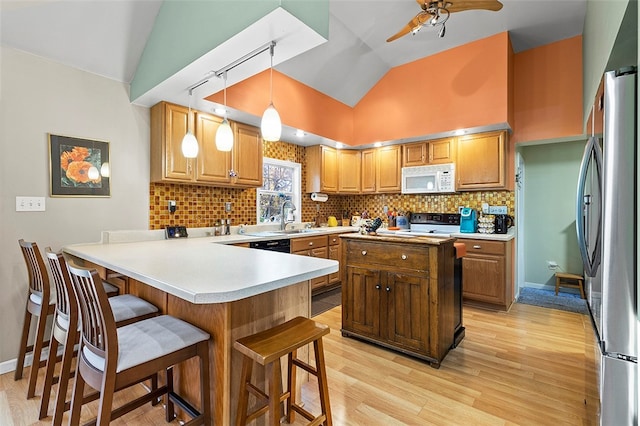 kitchen featuring kitchen peninsula, a kitchen breakfast bar, vaulted ceiling, pendant lighting, and white appliances