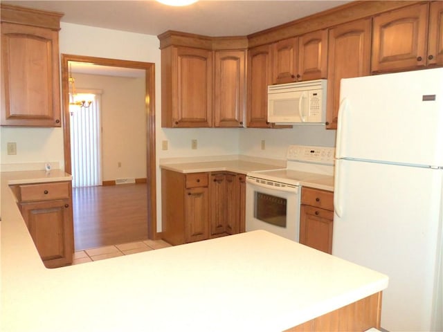 kitchen featuring light wood-type flooring, white appliances, kitchen peninsula, and an inviting chandelier