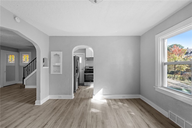 empty room featuring a textured ceiling, light hardwood / wood-style flooring, and plenty of natural light