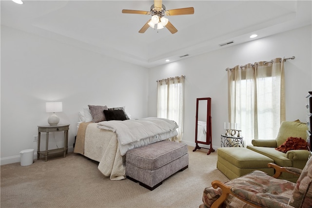 bedroom featuring a raised ceiling, light colored carpet, and ceiling fan