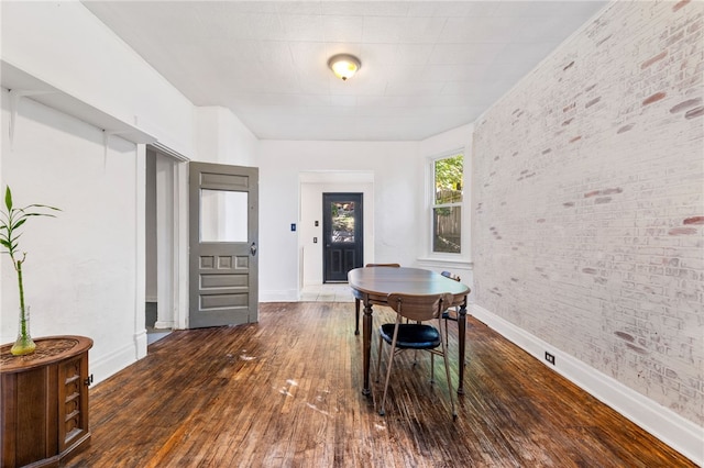 dining area with dark wood-type flooring and brick wall