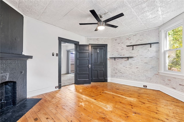 unfurnished living room with ceiling fan, hardwood / wood-style flooring, and brick wall