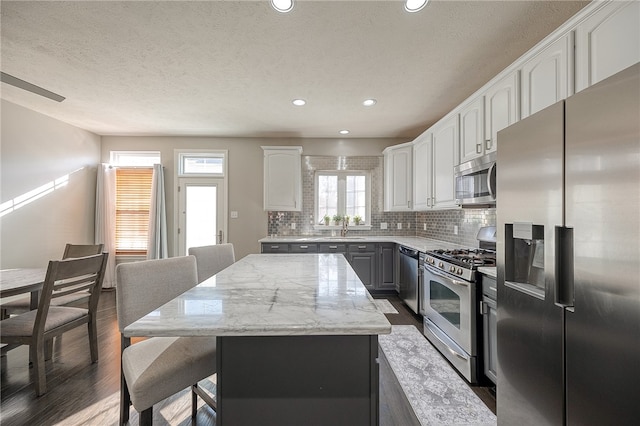 kitchen featuring a kitchen island, dark wood-type flooring, stainless steel appliances, white cabinetry, and light stone counters