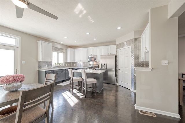 kitchen with appliances with stainless steel finishes, a kitchen island, white cabinetry, a breakfast bar, and dark hardwood / wood-style floors