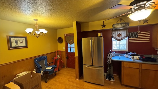 kitchen with ceiling fan with notable chandelier, a textured ceiling, pendant lighting, light hardwood / wood-style floors, and stainless steel refrigerator