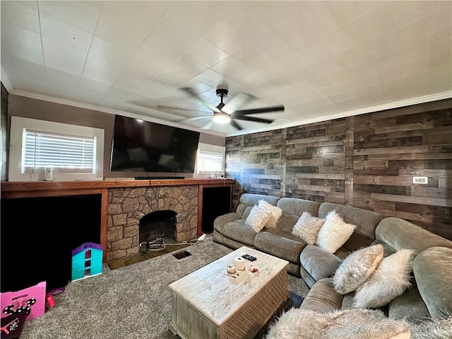 living room featuring ceiling fan, carpet flooring, ornamental molding, a stone fireplace, and wooden walls