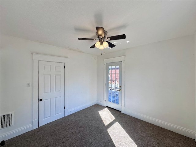 spare room featuring a textured ceiling, dark carpet, and ceiling fan