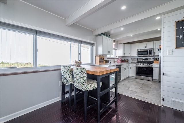 dining area featuring dark wood-type flooring, beam ceiling, sink, and plenty of natural light