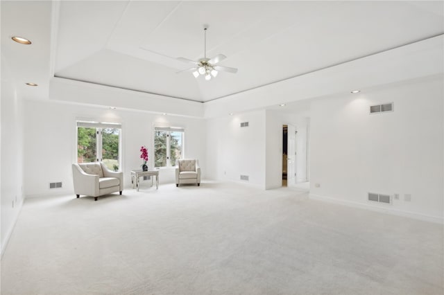 unfurnished room featuring ceiling fan, light colored carpet, and a raised ceiling