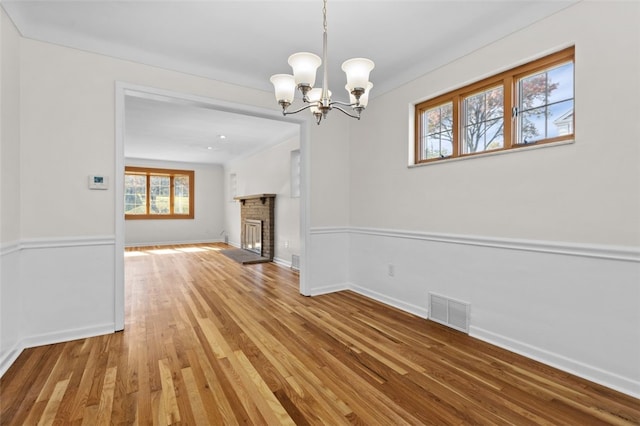 unfurnished dining area featuring hardwood / wood-style floors, a brick fireplace, and an inviting chandelier