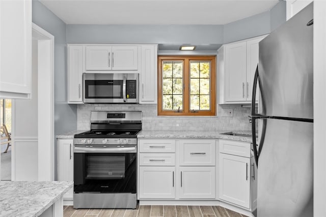 kitchen with light hardwood / wood-style flooring, stainless steel appliances, white cabinets, light stone counters, and tasteful backsplash