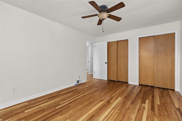 unfurnished bedroom featuring hardwood / wood-style floors, multiple closets, and ceiling fan