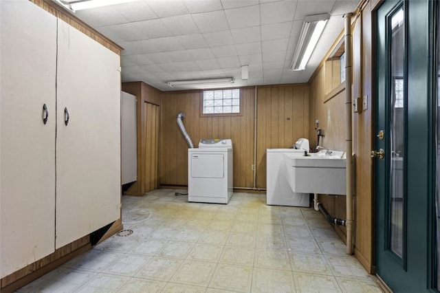 clothes washing area featuring wood walls, sink, and washer and clothes dryer