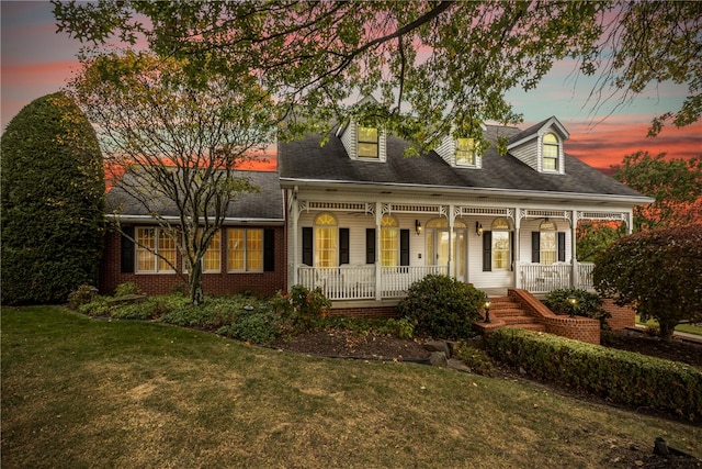 cape cod-style house featuring a porch and a yard