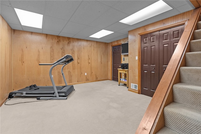 workout area with light carpet, a drop ceiling, and wooden walls