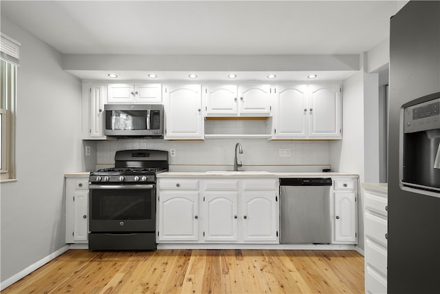 kitchen with tasteful backsplash, white cabinetry, sink, light hardwood / wood-style floors, and stainless steel appliances