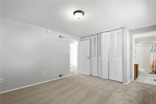 unfurnished bedroom with a closet, ensuite bathroom, and light colored carpet