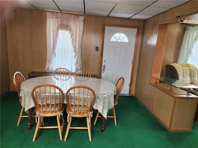 dining space with a drop ceiling, carpet flooring, and wood walls